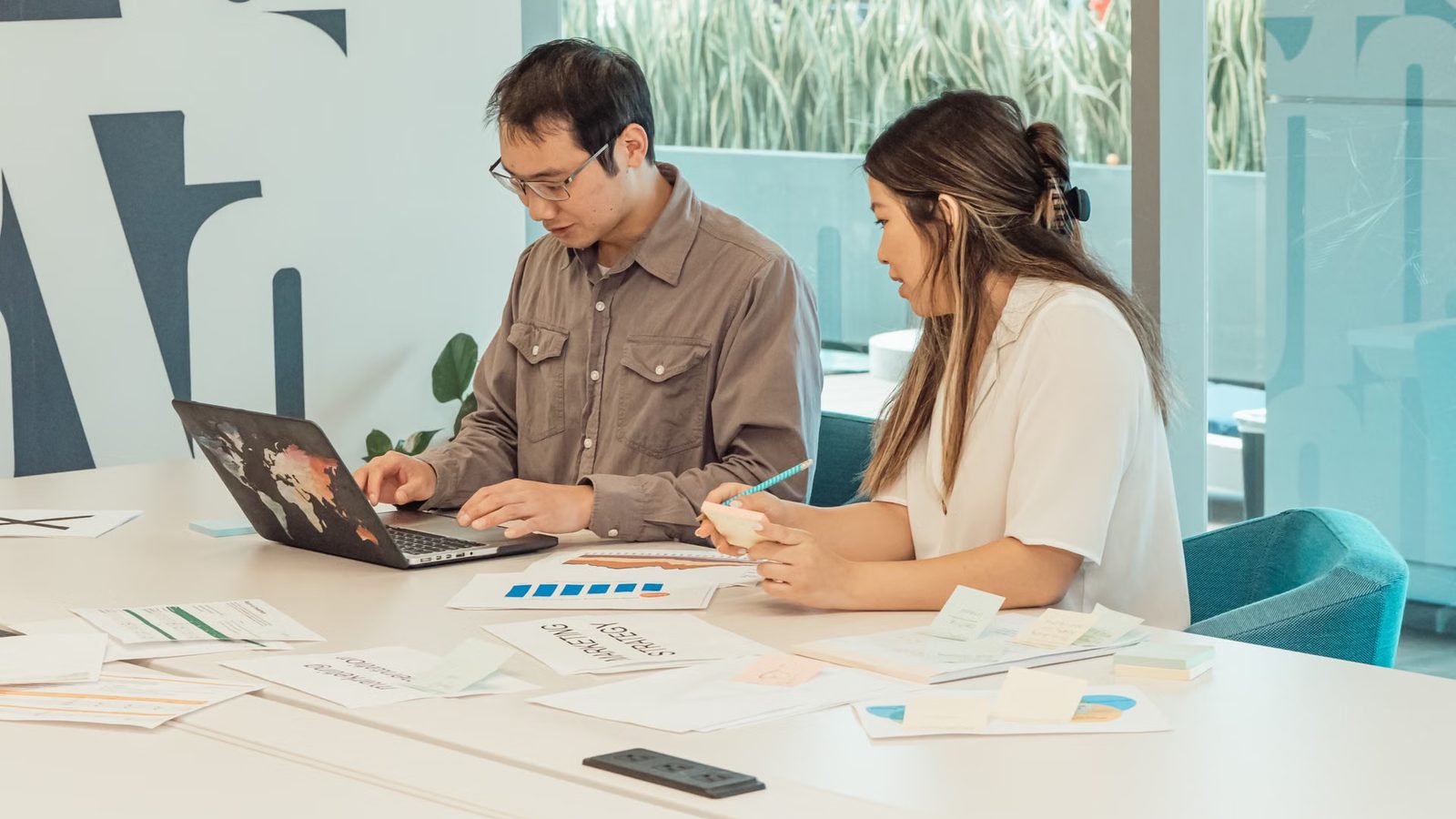 Two people leaning over a laptop at a shared desk